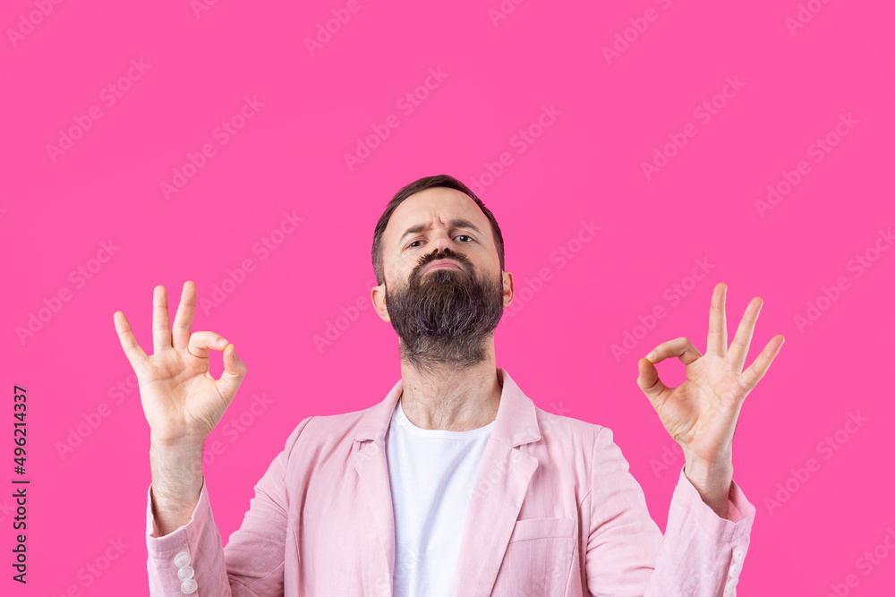 Portrait of a smiling young man in a pink jacket. Man showing ok gesture while standing in studio over isolated red background. Portrait of a smiling young man in a pink jacket. Man showing ok gesture while standing in studio over isolated red background.
