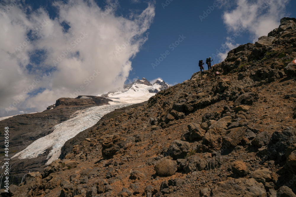 Alpine scenic. View of two hikers climbing up Tronador hill and glacier Castaño Overo in the Andes mountains in Patagonia Argentina. The rocky mountaintop and glacier ice field in a sunny day. 