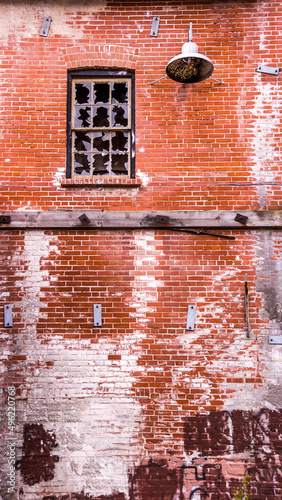Photography An old metal light sits beside a broken window high up on a red brick wall partially covered in graffiti