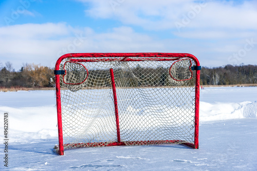 Photography A close up of a red ice hockey net on a frozen pond with snow banks behind on cloudy blue sky day