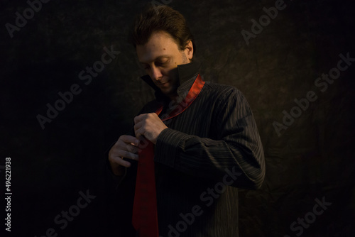 Retrato de hombre joven en estudio, estresado, preocupado y pensativo, con camisa oscura y corbata roja colgada al cuello sobre fodo negro. Bodegón. Naturaleza muerta. Joven caucásico. © Galdys V