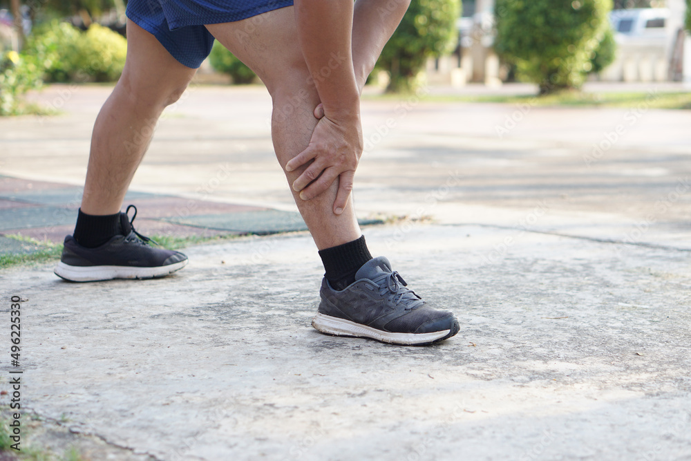 Runner uses hands to massage his sprain leg during exercise at the park. Concept : injury, sprain, painful from workout , exercise or sport.                