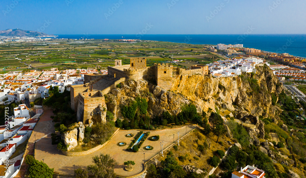 Picturesque autumn landscape with small Spanish town of Salobrena located on edge of stone cliff overlooking ancient fortified Arab castle..