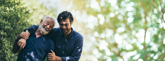 senior father hugging adult hipster son, have a happy feeling together, elderly caucasian person man or grandfather smiling with love in concept of family at home nature outdoor garden, banner space