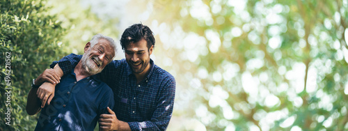 senior father hugging adult hipster son, have a happy feeling together, elderly caucasian person man or grandfather smiling with love in concept of family at home nature outdoor garden, banner space