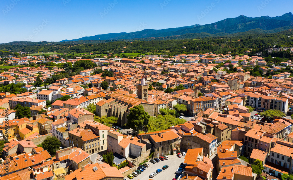 Scenic drone view of Prades summer cityscape surrounded by mountains overlooking bell tower of Saint-Pierre Church, Pyrenees-Orientales, France