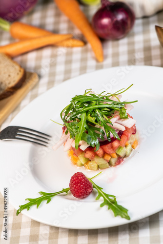Tartare of fresh diced vegetables and salads in a white plate decorated with a raspberry