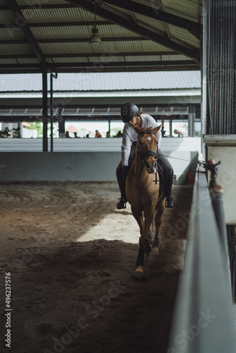 Young woman trains in horseback riding in the arena. Young Caucasian woman in formal clothing horseback riding across the sandy arena.  © Yuliya Kirayonak