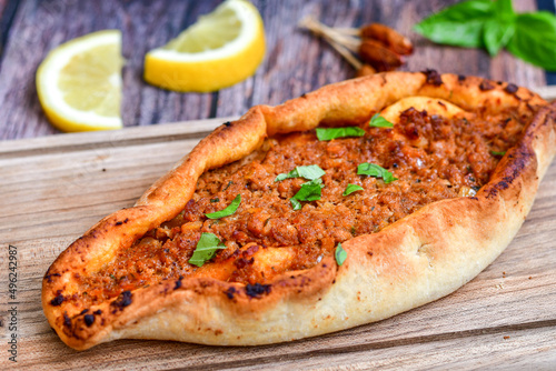  Traditional Turkish cuisine. Baked Pide dish with minced beef, tomatoes and herbs on wooden background. Turkish pizza pide
