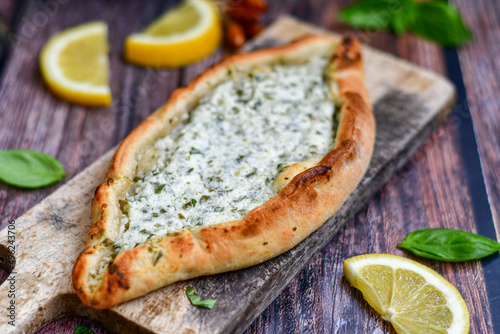  Traditional Turkish cuisine. Baked Pide dish with cheese and herbs on wooden background. Turkish pizza pide