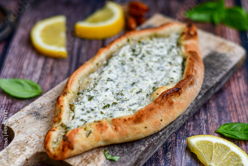  Traditional Turkish cuisine. Baked Pide dish with cheese and herbs on wooden background. Turkish pizza pide