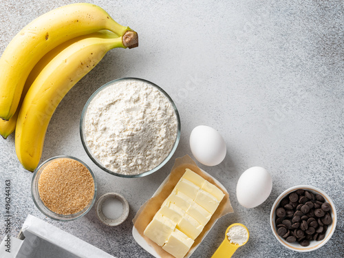 Banana bread (cake, pancakes or muffins) ingredients top view. Flour bowl, white eggs, butter, brown sugar, chocolate chips, bananas. Copy space.