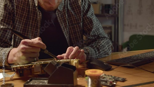 Employee fixes circuit board soldering microchip at workplace in shop close view. Repair of electrical equipment photo