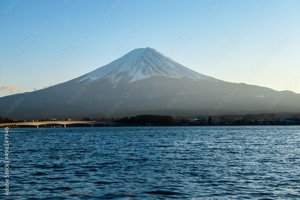 A close up view on Mt Fuji from the side of Kawaguchiko Lake, Japan. Soft colors of sunset - golden hour. Top of the volcano covered with a snow layer. Serenity and calmness. Calm lake's surface