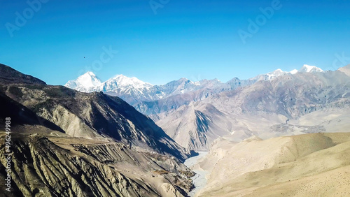 A panoramic view on dry Himalayan landscape. Located in Mustang region, Annapurna Circuit Trek in Nepal. In the back there is snow capped Dhaulagiri I. Barren and steep slopes. Harsh condition.