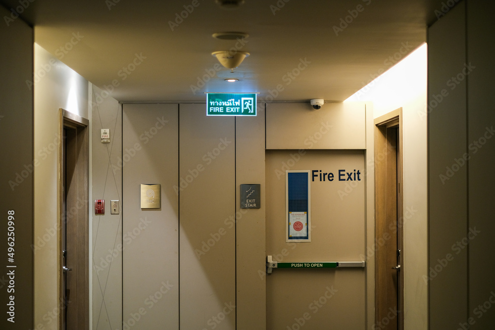 Emergency exit sign at the corridor in building. Green fire exit sign hanging on ceiling on dark