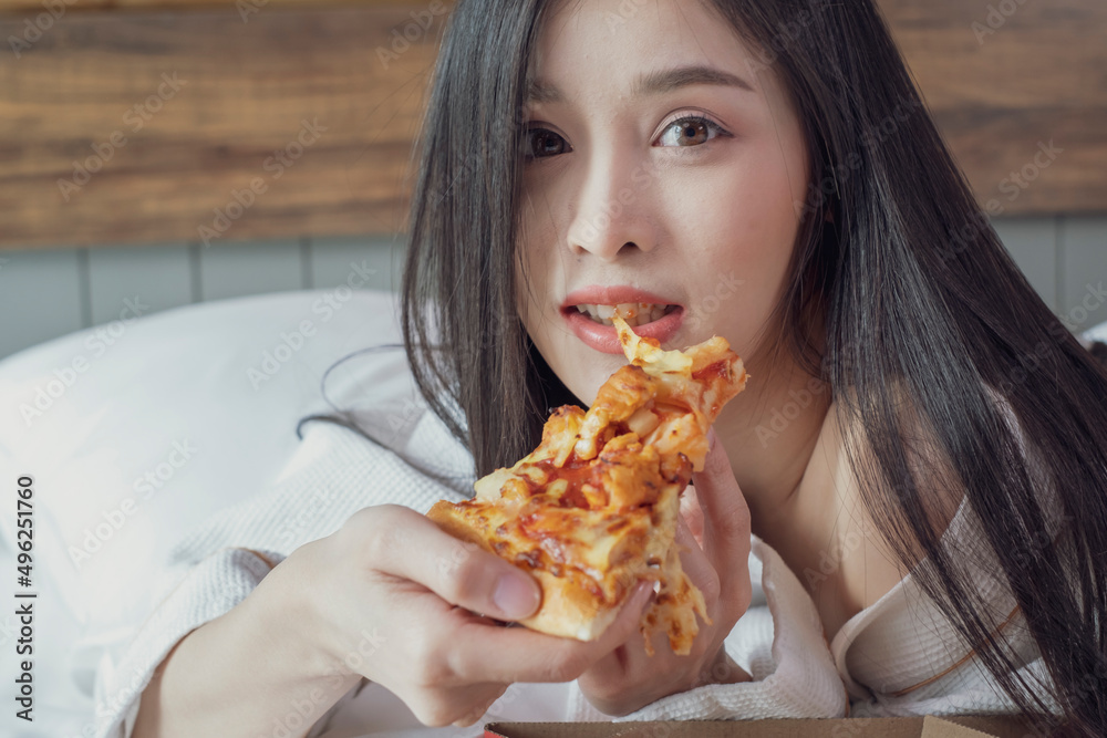 Happy young woman eating pizza on bed in hotel room. Beautiful female in hotel bed eating pizza and drink champagne. Happy young woman eating pizza on bed in hotel room. Beautiful female in hotel bed eating pizza and drink champagne.