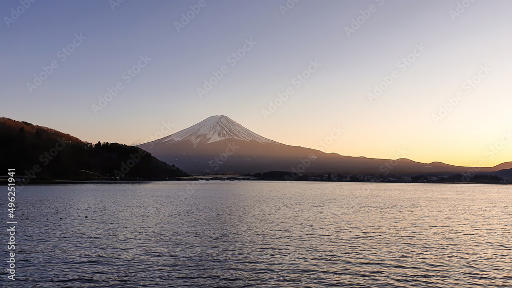 Idyllic view on Mt Fuji from the side of Kawaguchiko Lake, Japan. The mountain is surrounded by clouds. Calm surface of the lake moved by gentle wind. Serenity and calmness. Soft colors of the sunset