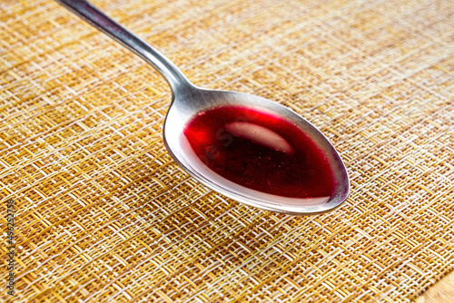 table spoon with red liquid on a light brown clipped background, kitchen concept photo