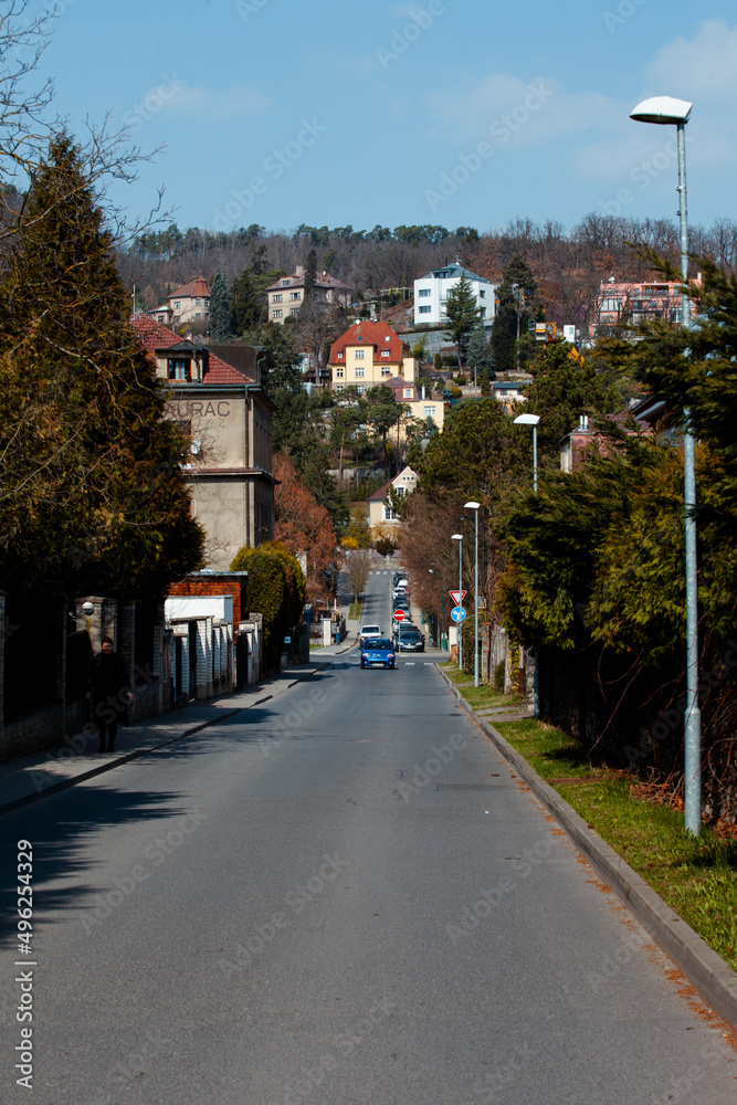 Urban perspective, a street that goes down and up. View of a street in a residential area. The weather is nice, sky is blue. The road is straight goes down and then up towards a house. 