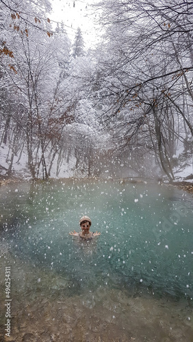 A girl in a hat swimming in a natural thermic spring in Maibachl, Austria during snowfall, winter. The thermic pool is located in the middle of the forest. Healing power of natural water. Relaxation
