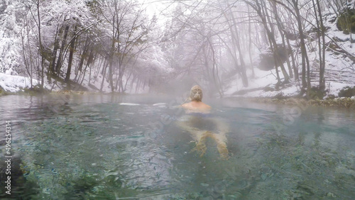 A man in a hat swimming in a natural thermic spring in Maibachl, Austria during snowfall, winter. The thermic pool is located in the middle of the forest. Healing power of natural water. Relaxation photo
