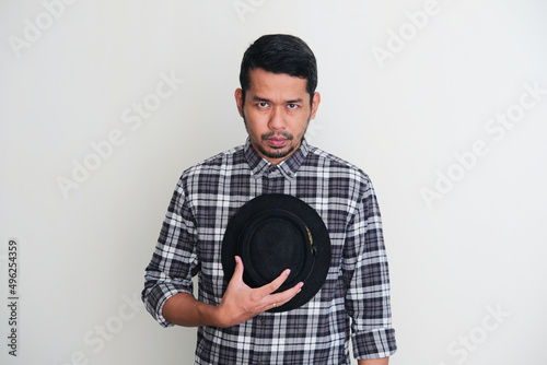 Adult Asian man put his hat on chest and showing sad expression when looking to camera photo