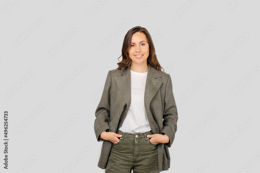 Young woman is smiling at the camera while standing with hands in pockets.