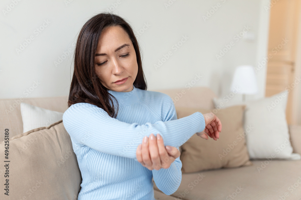 unhappy asian woman with elbow pain indoors. office syndrome health care concept. upset frowning asian lady confused looking at arms hurting sitting on couch at home in cozy bright apartment. unhappy asian woman with elbow pain indoors. office syndrome health care concept. upset frowning asian lady confused looking at arms hurting sitting on couch at home in cozy bright apartment.
