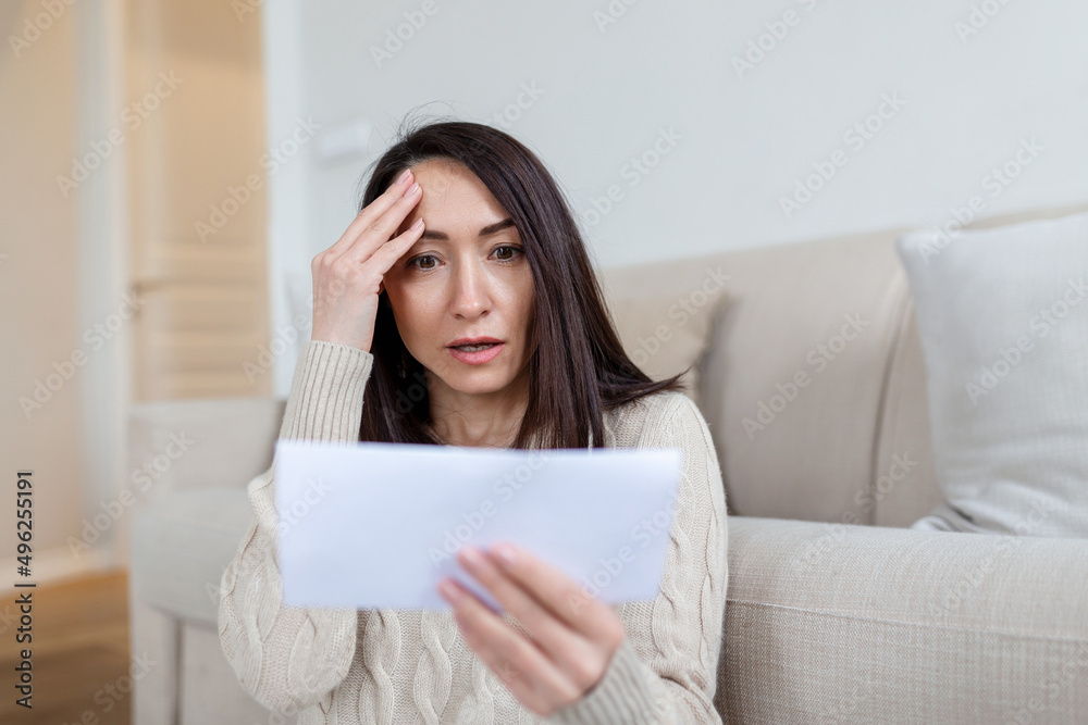 Portrait of a worried Asian woman looking at received letter at home. Beautiful woman with worried facial expression looking at received mail. Portrait of a worried Asian woman looking at received letter at home. Beautiful woman with worried facial expression looking at received mail.