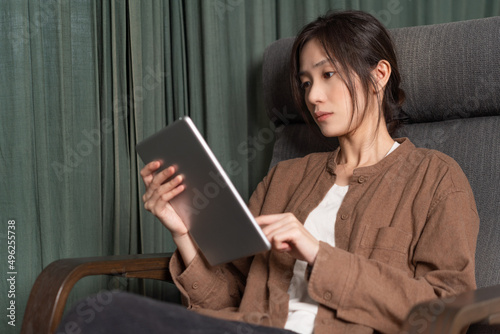 Asian woman holding a tablet is sitting in a rocking chair 