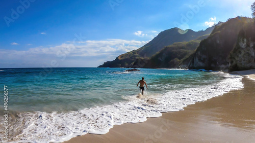 A man running along the shore, chasing the waves on idyllic Koka Beach. Hidden gem of Flores, Indonesia. He is having a lot of fun, collecting happy moments. Adventure and discovering while travelling photo