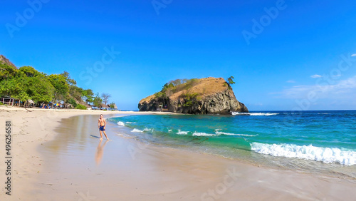 A man standing on the shore of idyllic Koka Beach. Hidden gem of Flores, Indonesia. There is a big headland behind him. Clear and bright day. Adventure and discovering while travelling photo
