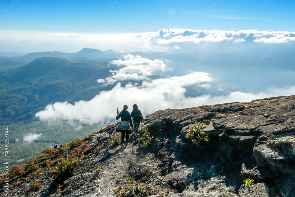A couple walking down the steep side of volcano Inierie in Bajawa, Flores, Indonesia. They are enjoying the beautiful view on volcanic island. They walk down very fast, surrounded by clouds.