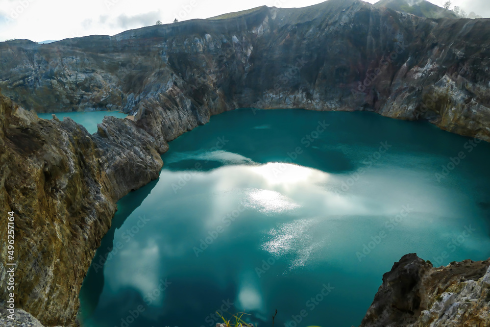 Obraz premium Close up view on the Kelimutu volcanic crater lakes in Flores Indonesia. Lakes are shining with many shades of turquoise and blue. Sun shines through clouds. Barren and sharp slopes of volcanic crater