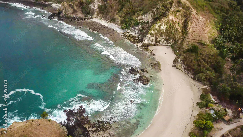 Top-down drone shot of an idyllic Koka Beach. Hidden gem of Flores, Indonesia. Beauty in the nature. Calm waves washing the cliff's slopes. Serenity and calmness. Beach surrounded by high, green hills