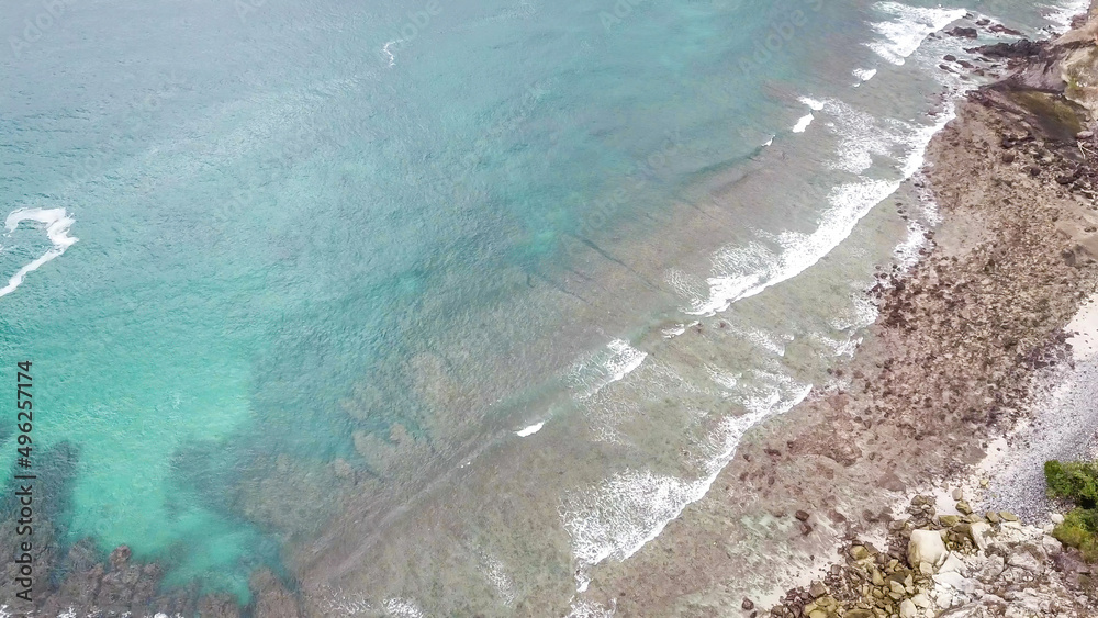 Obraz premium Top-down drone shot of an idyllic Koka Beach. Hidden gem of Flores Indonesia. Beauty in the nature. Calm waves washing the cliff's slopes. Serenity and calmness. There are a lot of boulders in the sea