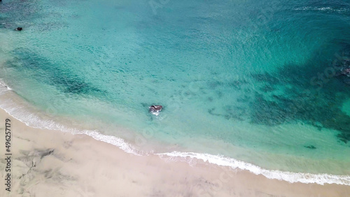 Top-down drone shot of an idyllic Koka Beach. Hidden gem of Flores Indonesia. Beauty in the nature. Calm waves washing the sandy shore gently. Serenity and calmness. There are some boulders in the sea © Chris