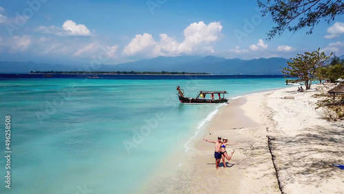 Fototapeta Naklejka Na Ścianę i Meble -  A couple standing on white sand beach on Gili Air, Lombok, Indonesia. Beautiful and clear sea water. There is a boat anchored to the beach. In the back visible Mount Rinjani. Holidays paradise.