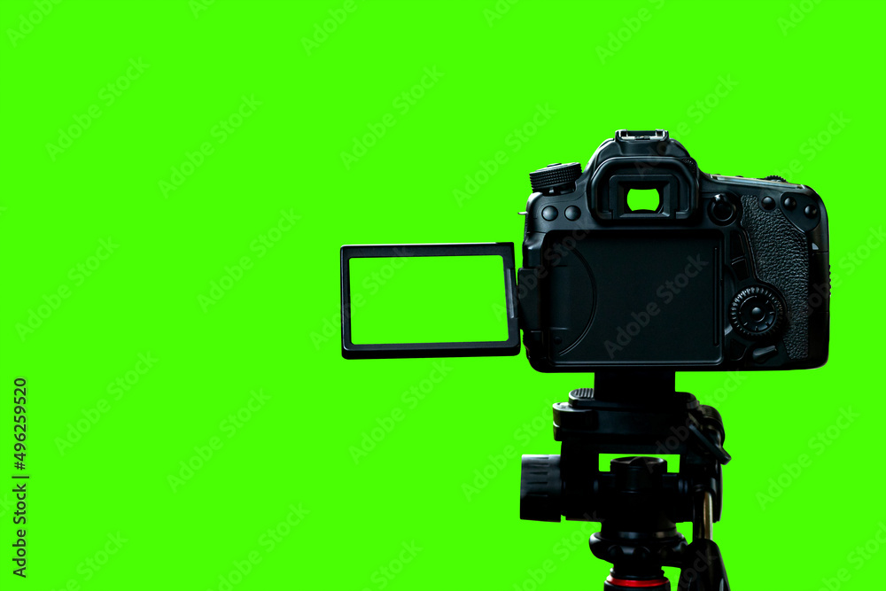 The DSLR. camera with empty screen on the tripod, isolated on green