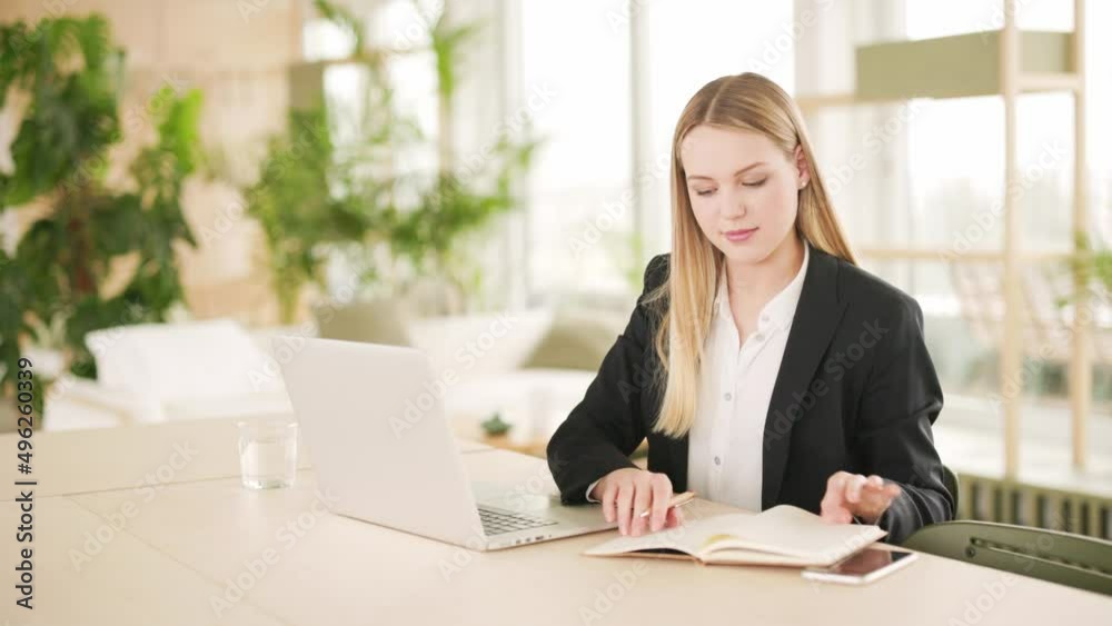Young woman sitting in office with laptop writing in notebook Young woman sitting in office with laptop writing in notebook