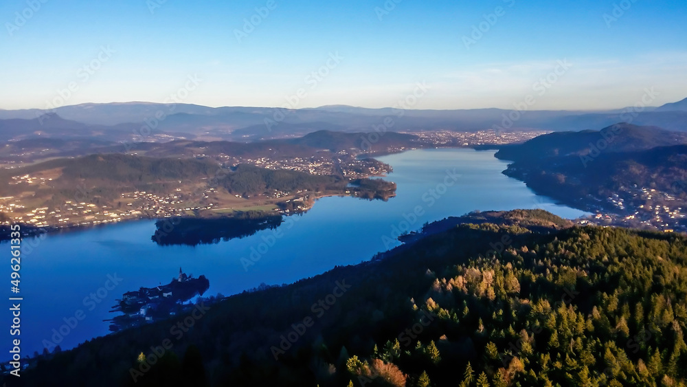 A view on the Woerthersee lake from the observation deck of Pyramidenkogel Tower. Lake is reflecting the last beams of sun for this day. Golden hour. The surrounding hills are shining gold.
