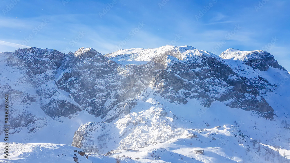 A beautiful and serene landscape of mountains covered with snow. Thick snow covers the steep slopes. Clear weather. The mountain massive looks pretty dangerous. Possibility of an avalanche.