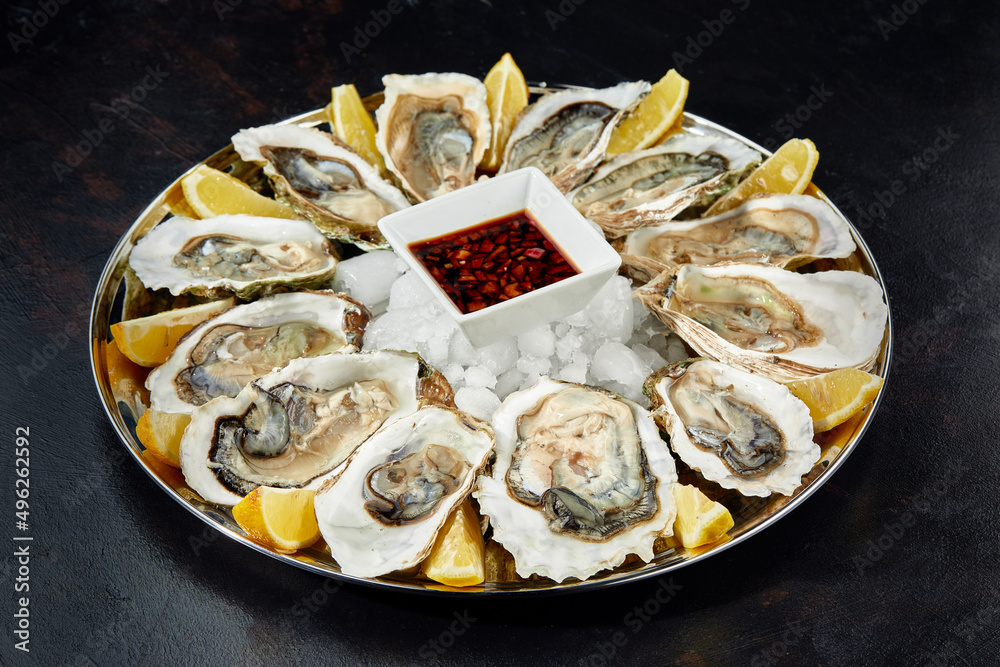 Oysters with lemon served on black round platter. Luxury delicatessen seafood.