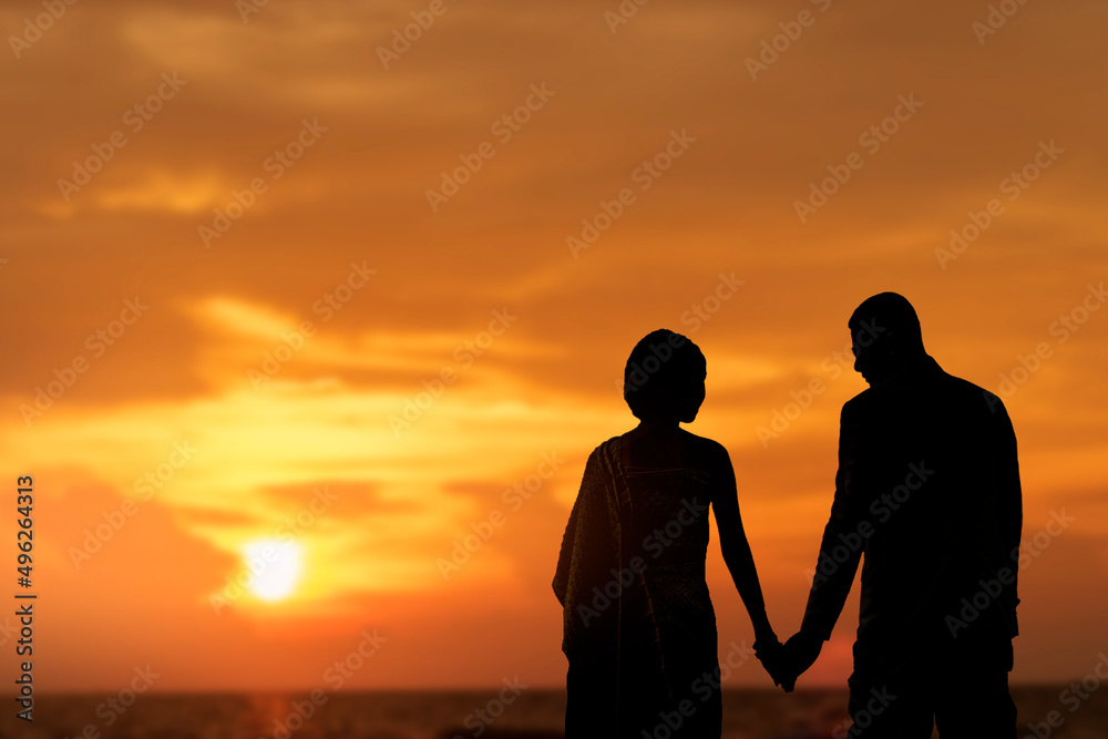 silhouette Couple, man and woman, stand hand in hand on the beach at sunset.
