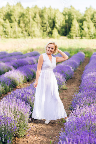 An elderly woman walks in a field of lavender. Beautiful senior in a white dress in lavender