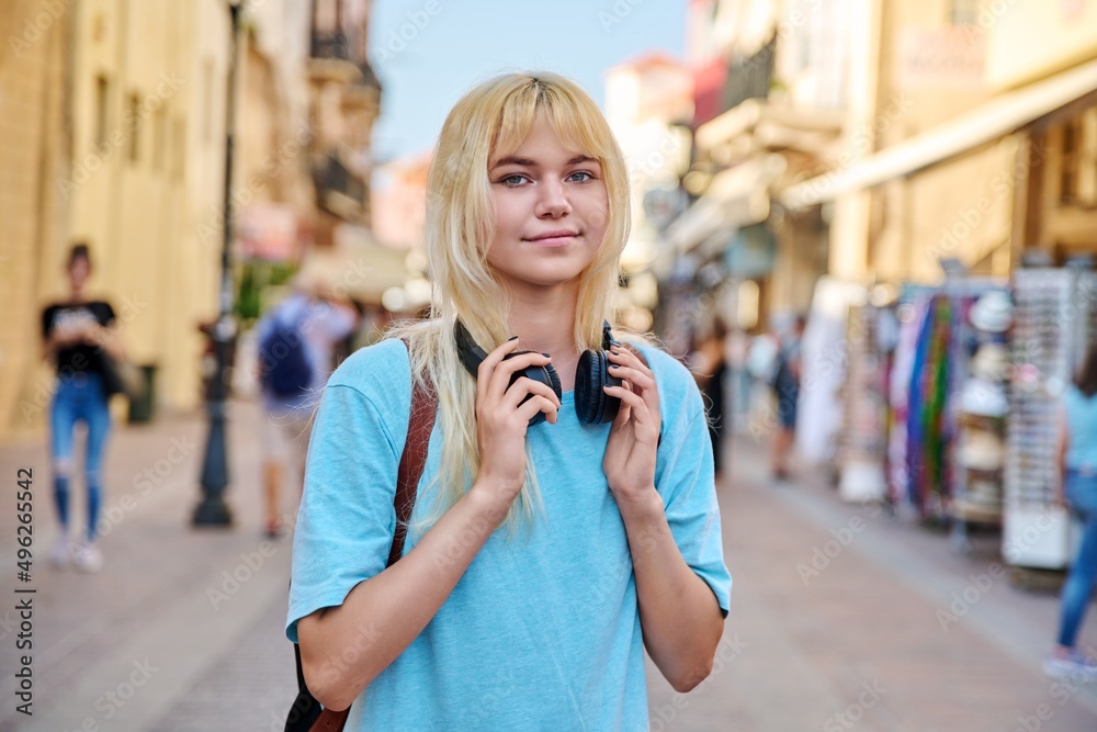 Fototapeta premium Young woman in headphones with backpack on street of tourist city