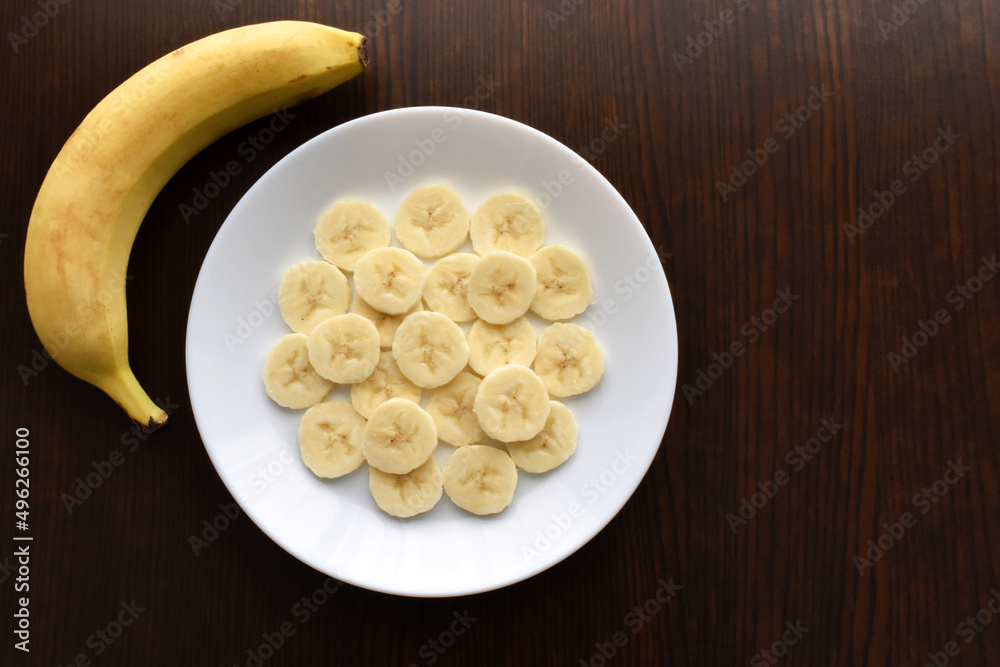 Banana slices on a white plate. Copy space is on the right side. Flat lay top view photo. Food from above concept. Banana slices on a white plate. Copy space is on the right side. Flat lay top view photo. Food from above concept.