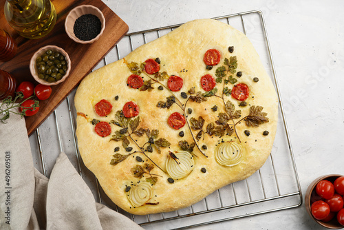 Floral painting focaccia, italian garden flatbread art with parsley, tomatoes, onions, sesame seeds and capers on light grey background