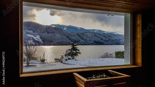 Alpine sauna with the view on the lake and the mountains. Under the window there is a furnace, warming the stones. Mountains covered with snow. Relaxation and chill in winter wonderland.